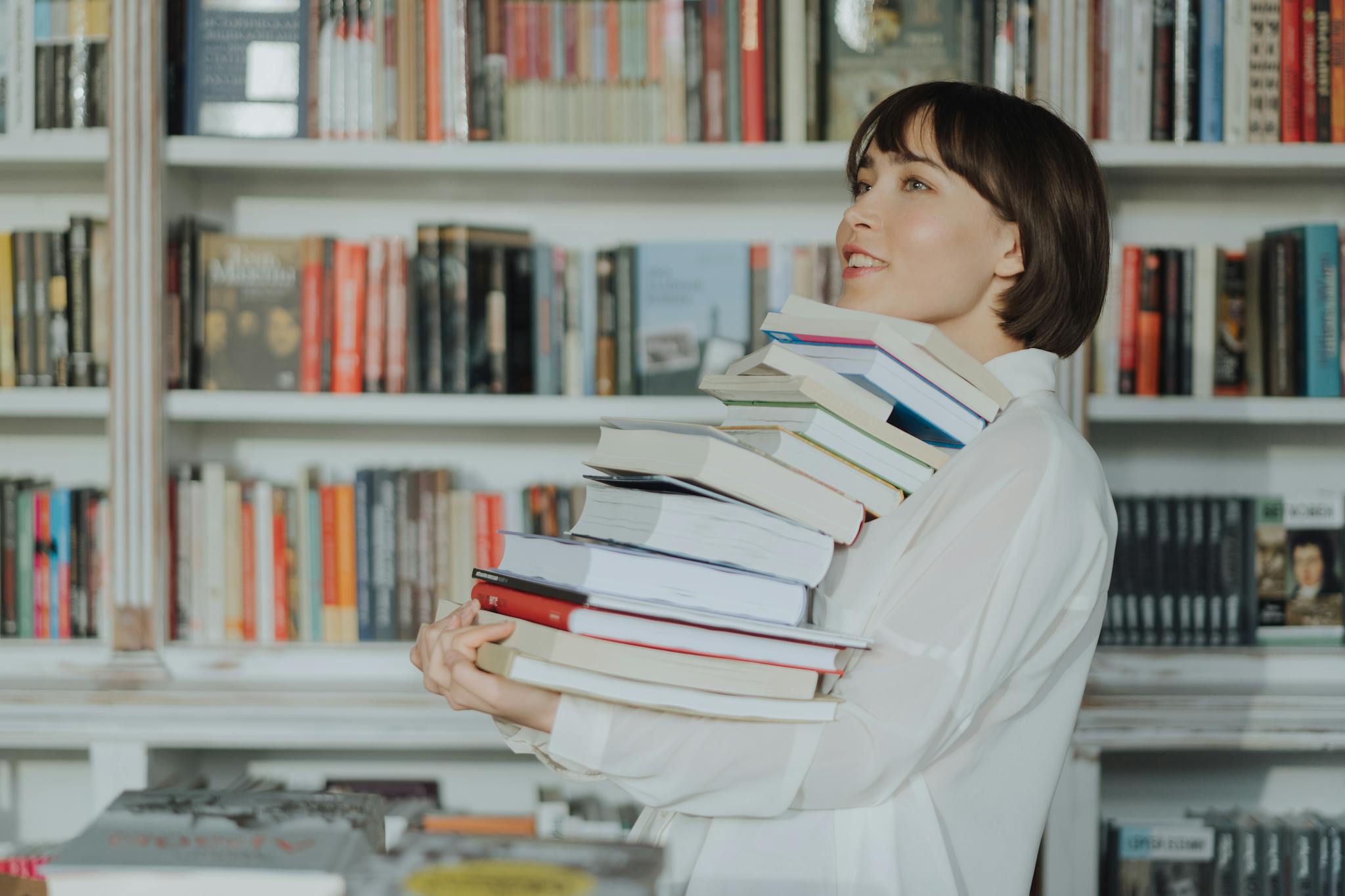 A woman joyfully holds a pile of books in a library, embodying the love of reading and learning.