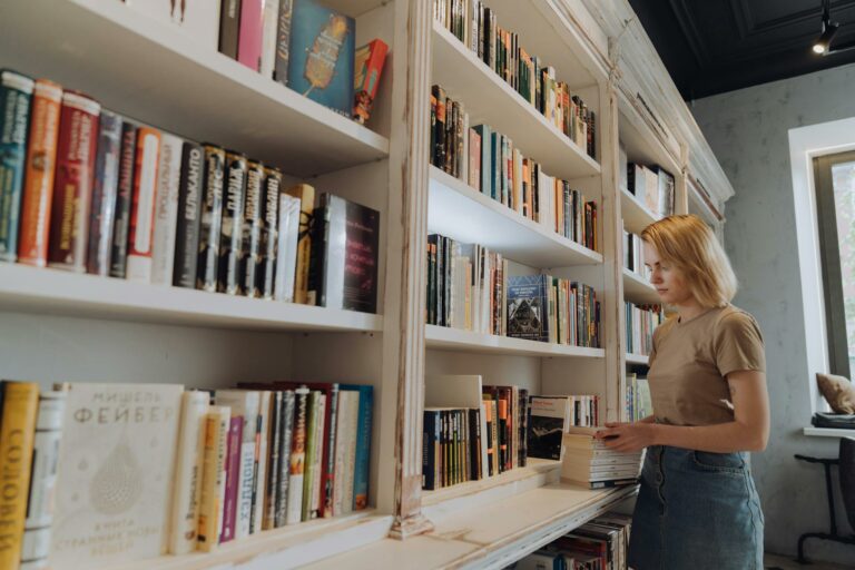 A woman organizing books on a bookshelf in a library setting.