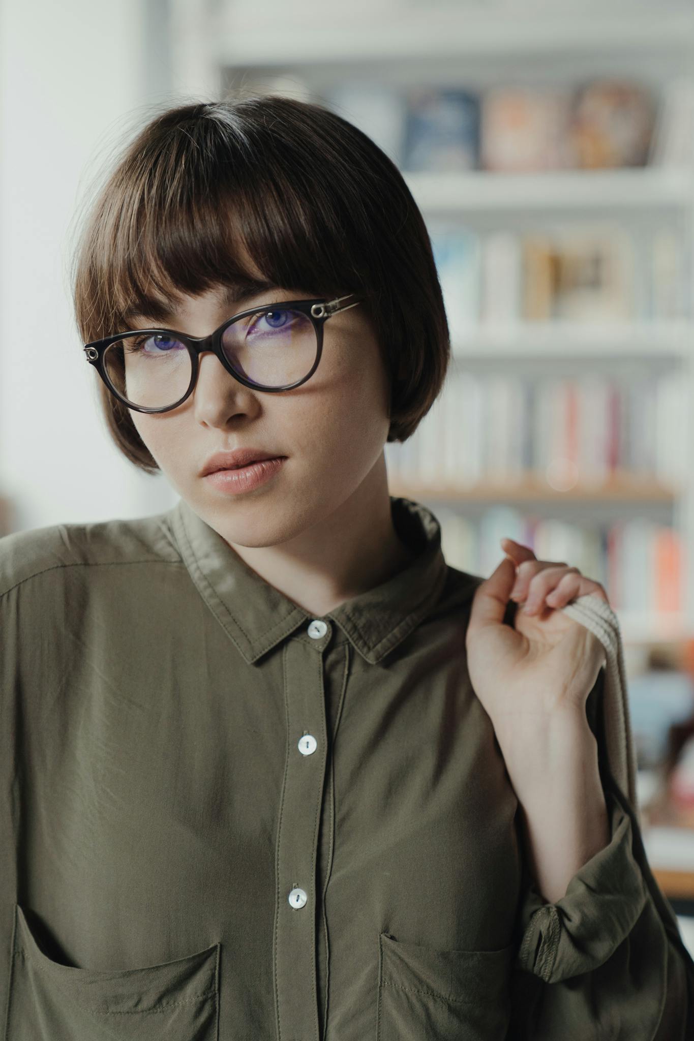Portrait of a young woman wearing glasses, standing in a library, conveying intelligence and leisure.