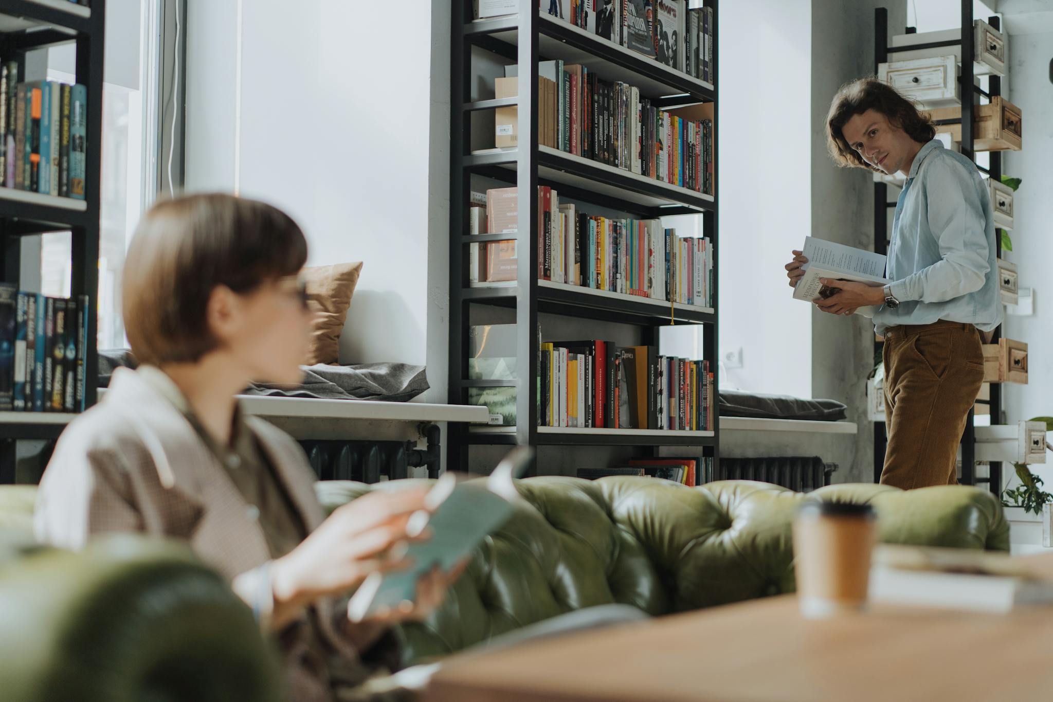 Young adults reading in a modern library with bookshelves, creating a cozy intellectual atmosphere.
